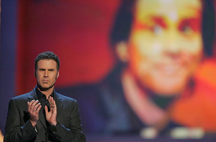 Comedian speaking at a podium with a large blurred image of Jim Carrey behind, highlighting net worth and mansion drama.