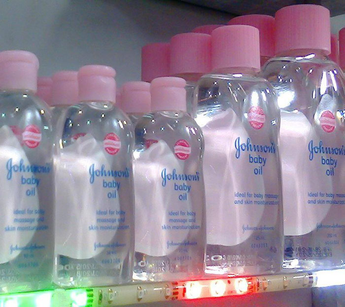 Bottles of Johnson&rsquo;s baby oil with pink caps lined up on a shelf, focusing on skin moisturizer and massage use.