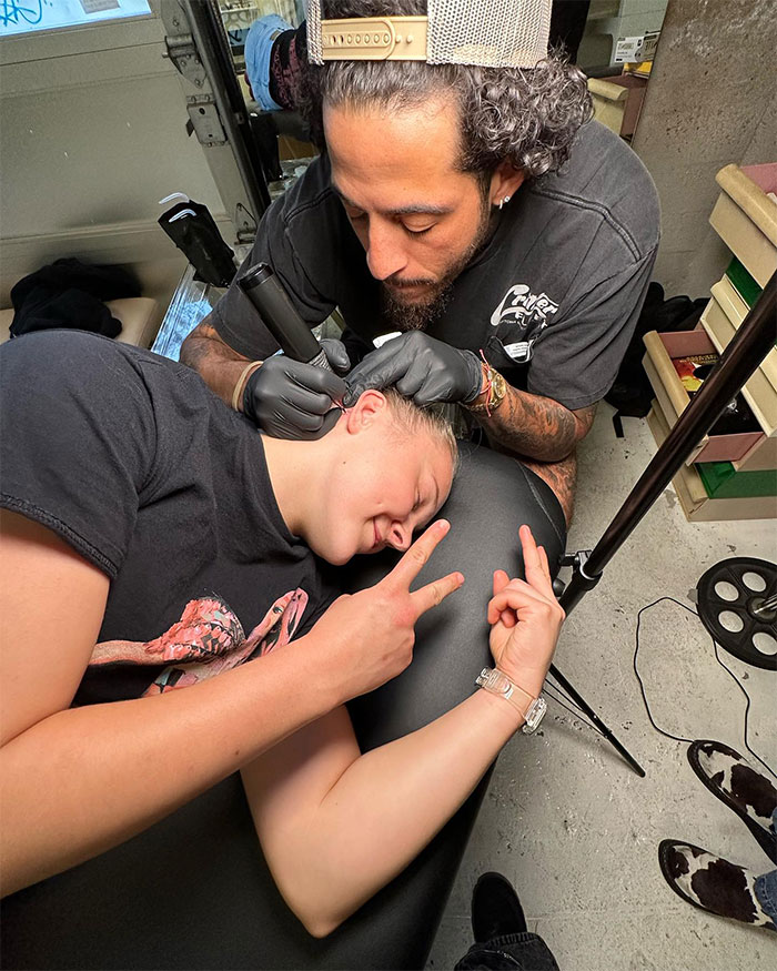 Jojo Siwa getting a tattoo on her head from a tattoo artist in a studio, showcasing her tattoos so far.