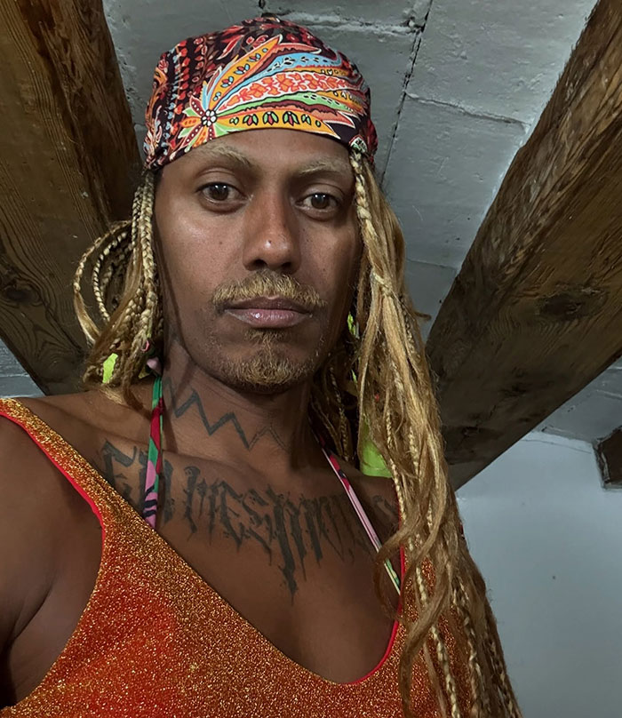 Person with long braided hair and a colorful headscarf wearing a sparkling top, breaking Cannes dress code with mass applause.