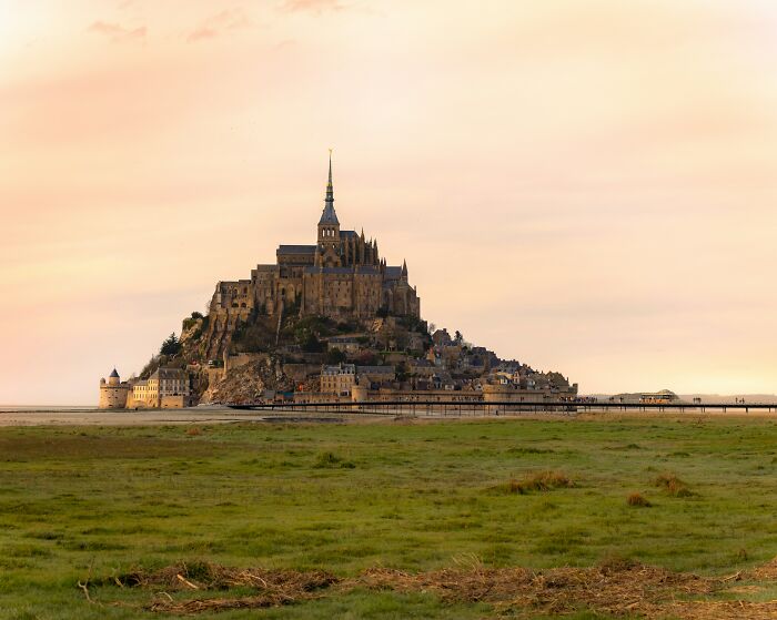 Mont Saint-Michel at sunset with a wide green field in the foreground, showcasing one of the must-see wonders.