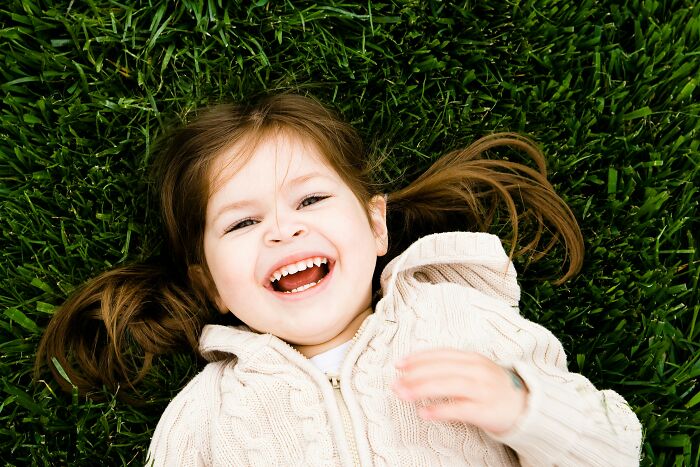 Happy young girl with pigtails lying on green grass, illustrating hilariously bad names that raise questions about parenting choices.