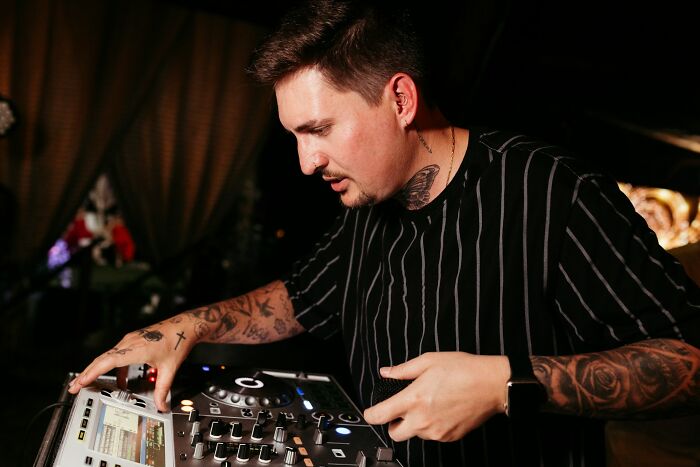 Man with tattoos using a DJ controller at a nighttime event, revealing industry secrets behind closed doors.