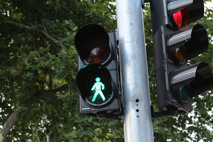 Green pedestrian walk signal on a traffic light pole symbolizing precautionary safety steps that saved lives.