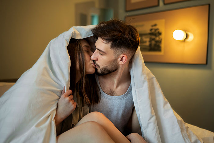 Couple sharing a kiss under a blanket in a cozy bedroom, illustrating personal precautions that saved their lives.