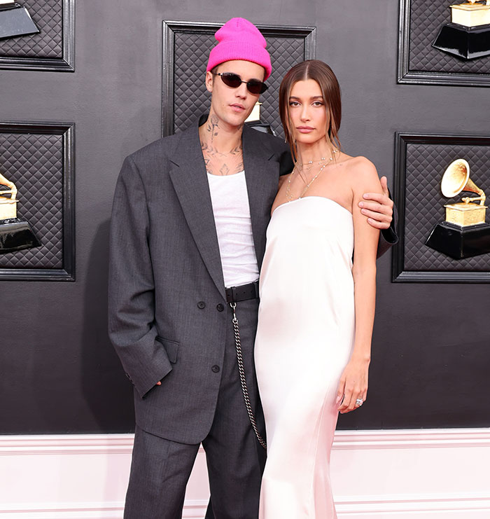Justin Bieber wearing a pink beanie and sunglasses with Hailey Baldwin posing at a music awards event.