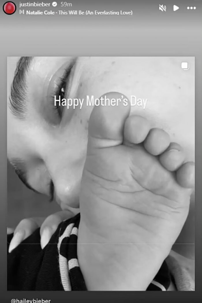 Black and white close-up of Justin Bieber&rsquo;s face near a baby&rsquo;s foot with a Happy Mother's Day message on screen.