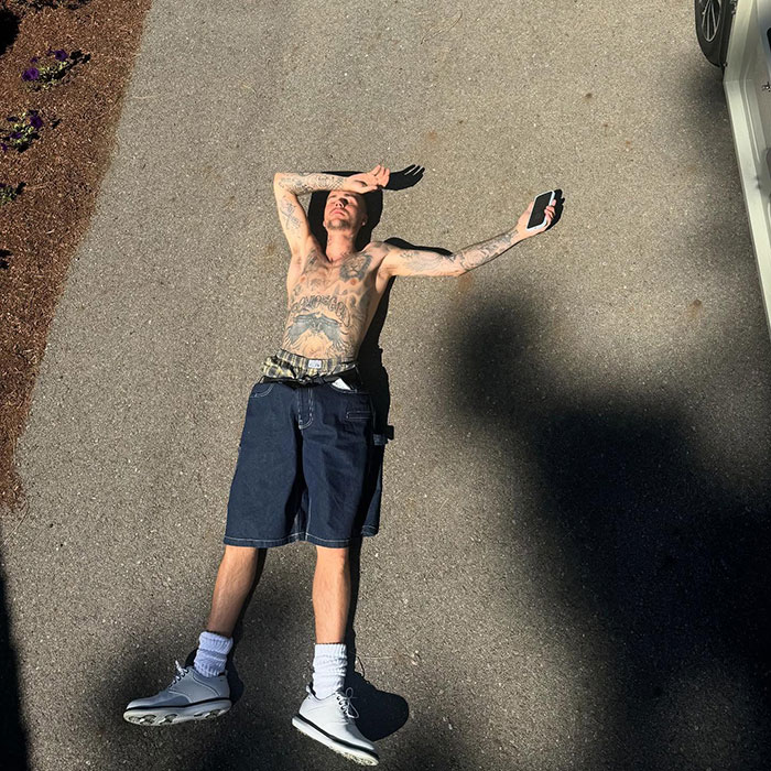 Justin Bieber lying shirtless on pavement with tattoos, holding a phone, sparking a fiery parenting debate over smoking.