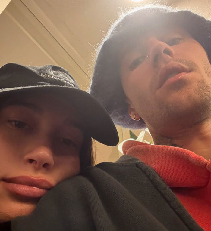Justin Bieber and a woman in casual hats, capturing a close-up selfie indoors with neutral expressions.