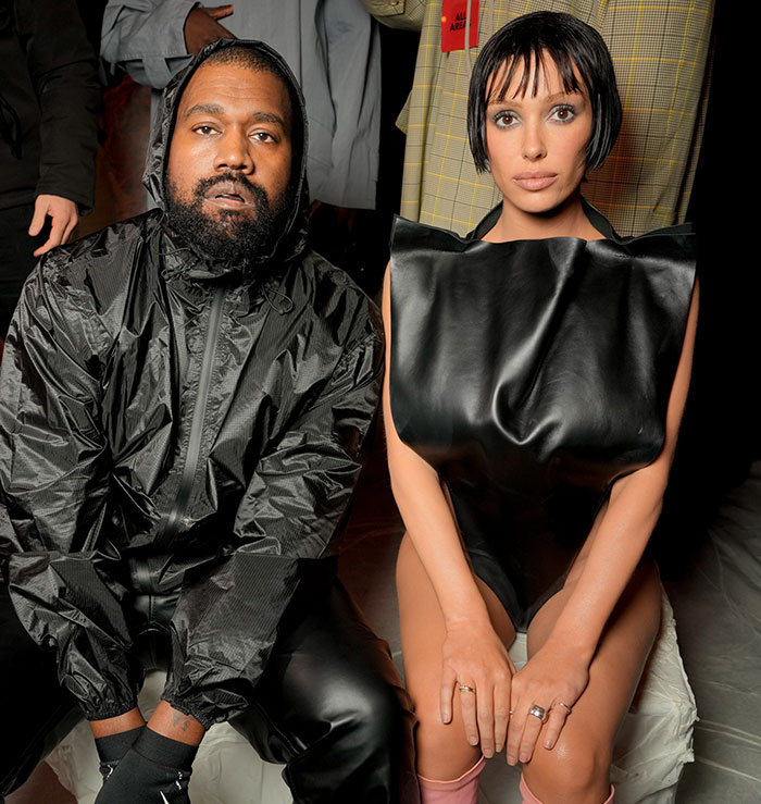 Bianca Censori posing in edgy black outfit while public calls for arrest over alleged public indecency incident.