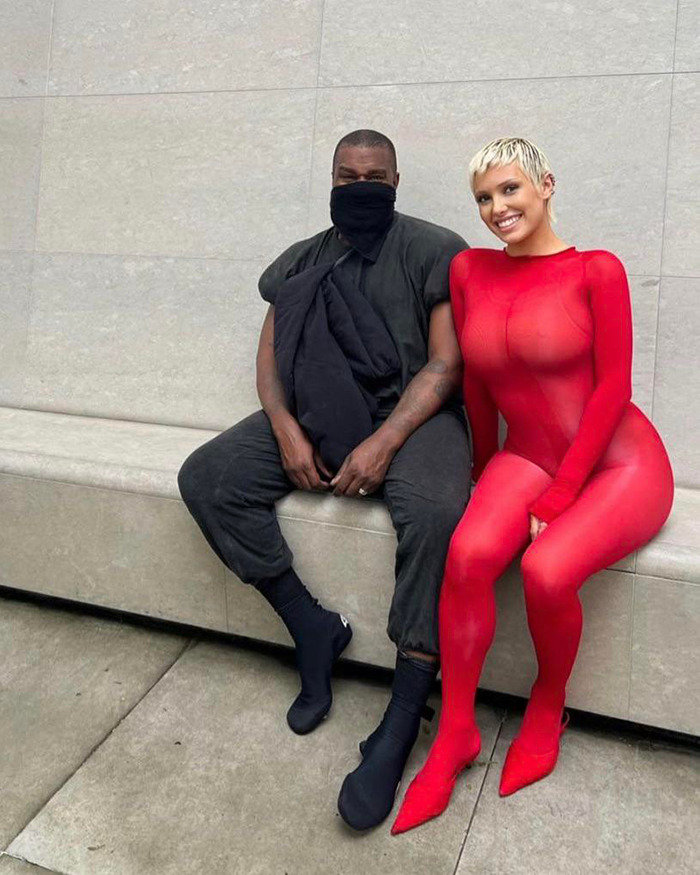 Kanye West sitting next to Bianca Censori in a red outfit, sharing a post about being subservient to her master.