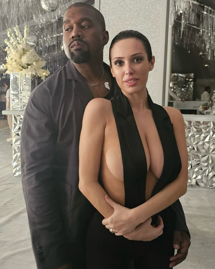Kanye West and Bianca Censori posing together indoors with reflective and floral decor in the background.