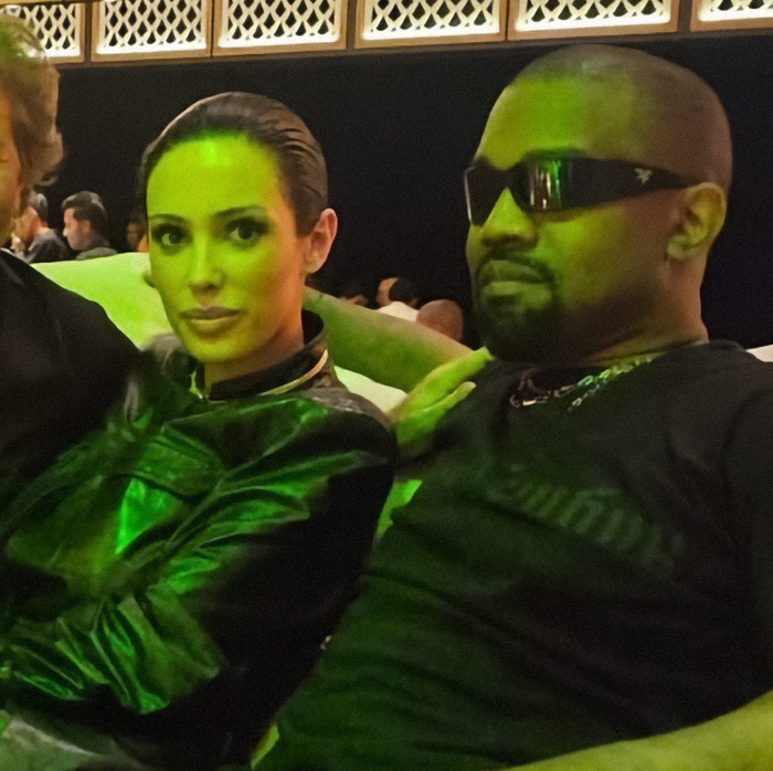Kanye West and Bianca Censori sitting together in a dimly lit venue, highlighting Kanye West subservient post.