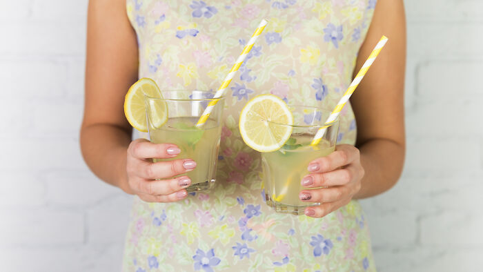 Person holding two glasses of lemonade with lemon slices and striped straws, connected to unhinged parents diabolical theme.