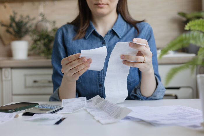 Woman in denim shirt tearing receipts in frustration, depicting unhinged parents dealing with diabolical financial stress.