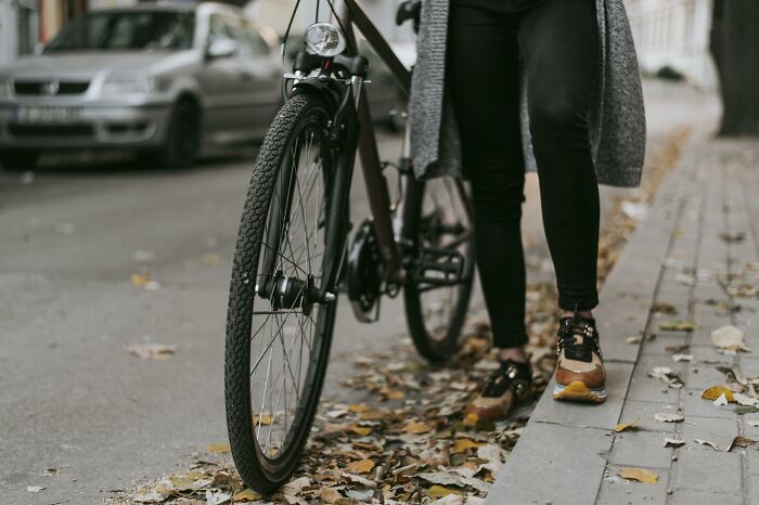Person standing next to a bicycle on a leaf-covered city sidewalk, illustrating unhinged parents in a diabolical situation.