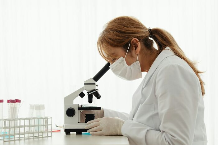 Scientist in a lab coat and mask using a microscope, illustrating company secrets shared after no longer working there.
