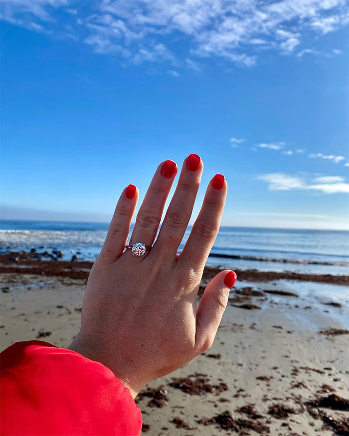 Hand with red painted nails showing engagement ring at the beach, related to Karoline Leavitt&rsquo;s husband Nicholas Riccio.