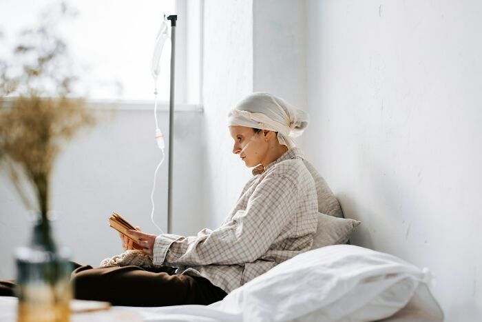 Young patient with IV drip, wearing a headscarf, resting in bed and reading, illustrating stories of good or bad genes.