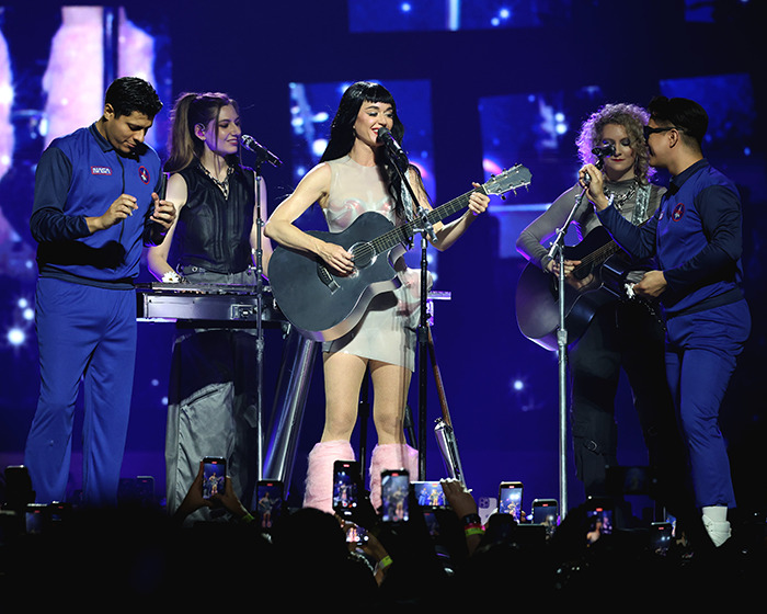 Katy Perry performing live with band members during her astronaut-themed world tour concert on stage with fans recording. Katy Perry performing live with band members during her astronaut-themed world tour concert on stage with fans recording.