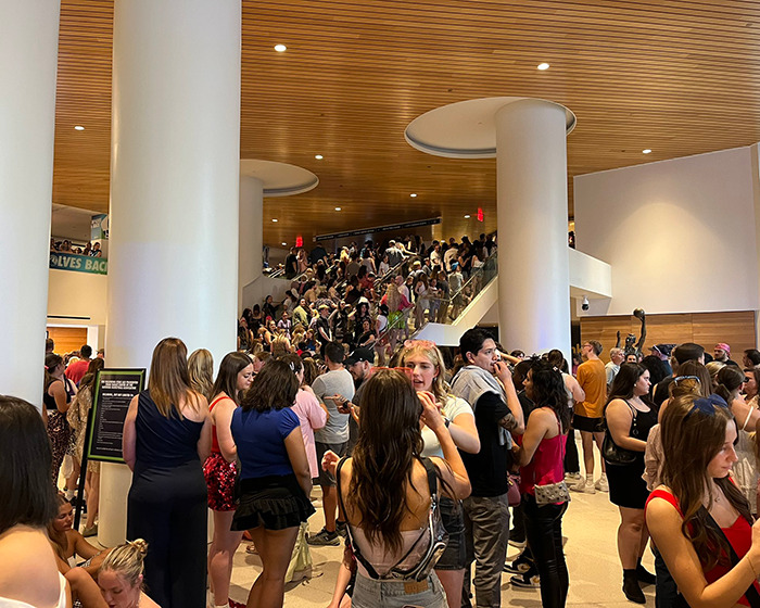 Crowd gathered at event venue with people socializing near large white columns during Katy Perry world tour setback. Crowd gathered at event venue with people socializing near large white columns during Katy Perry world tour setback.