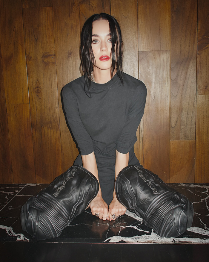 Katy Perry seated on floor in black outfit and oversized boots, reflecting a moment during her world tour setback. Katy Perry seated on floor in black outfit and oversized boots, reflecting a moment during her world tour setback.