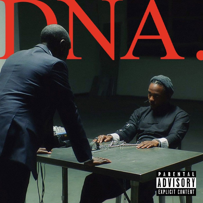 Kendrick Lamar seated and handcuffed at a table in a dark room during a tense interrogation scene with a standing man.