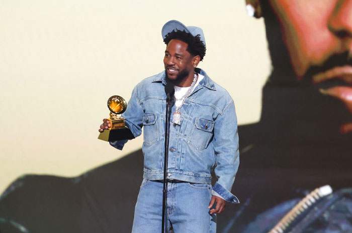 Kendrick Lamar holding a Grammy award onstage, showcasing his rising net worth and music career success.