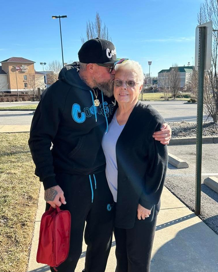 Man wearing black hoodie and cap kissing older woman on the cheek outside, related to lottery win and arrest news. Man wearing black hoodie and cap kissing older woman on the cheek outside, related to lottery win and arrest news.