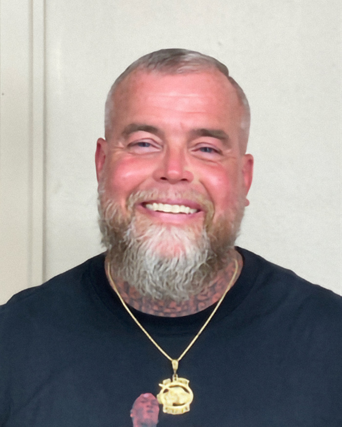 Smiling man with gray beard wearing a black shirt and gold necklace after winning lottery, facing legal troubles soon after. Smiling man with gray beard wearing a black shirt and gold necklace after winning lottery, facing legal troubles soon after.