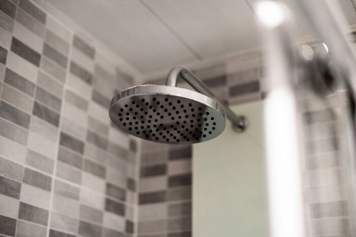 Close-up of a modern showerhead in a tiled bathroom, illustrating aspects of morally questionable actions by netizens.