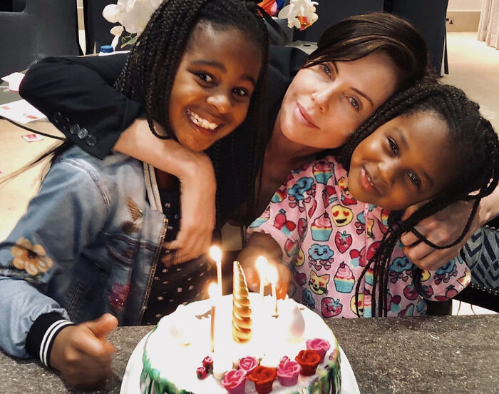 Charlize Theron with her children smiling by a lit birthday cake, showing family moments and playful respect dynamics.