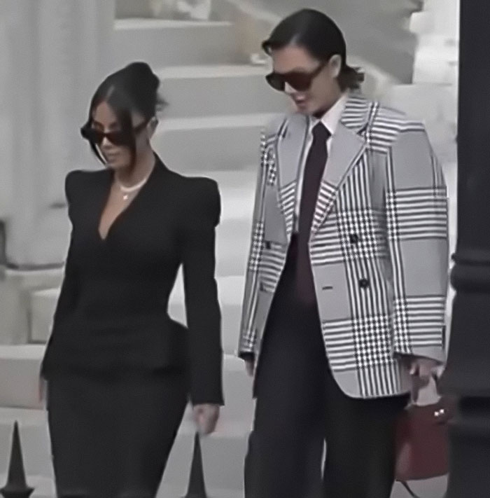 Kim Kardashian wearing a black dress and sunglasses, walking with a companion in Paris during jewelry heist trial.