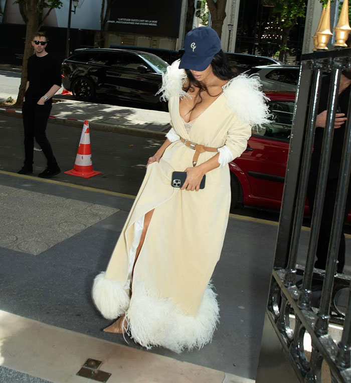 Kim Kardashian wearing a feathered beige dress and baseball cap while attending jewelry heist trial in Paris.