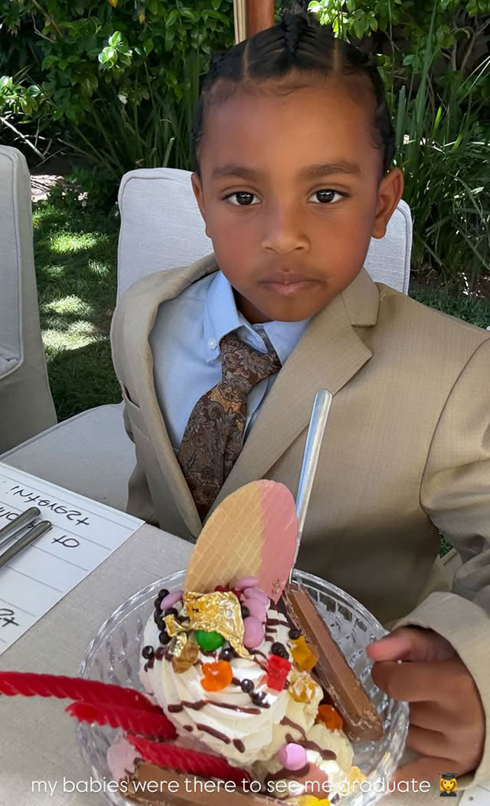 Young boy dressed in a suit enjoying dessert at an outdoor celebration for Kim Kardashian graduating law school.