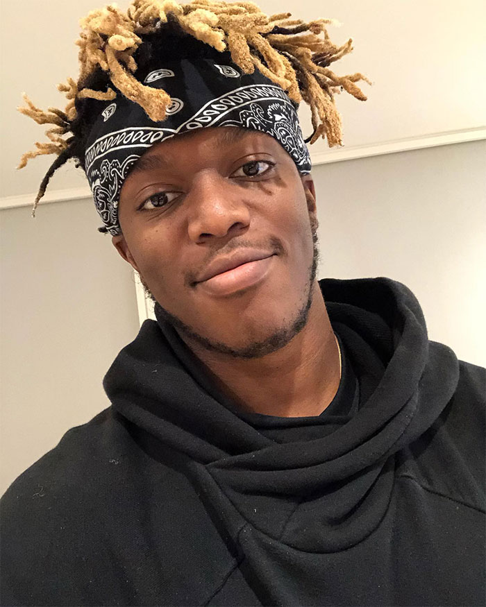 KSI smiling indoors wearing a black hoodie and patterned bandana, highlighting KSI&rsquo;s net worth and Prime stake success.