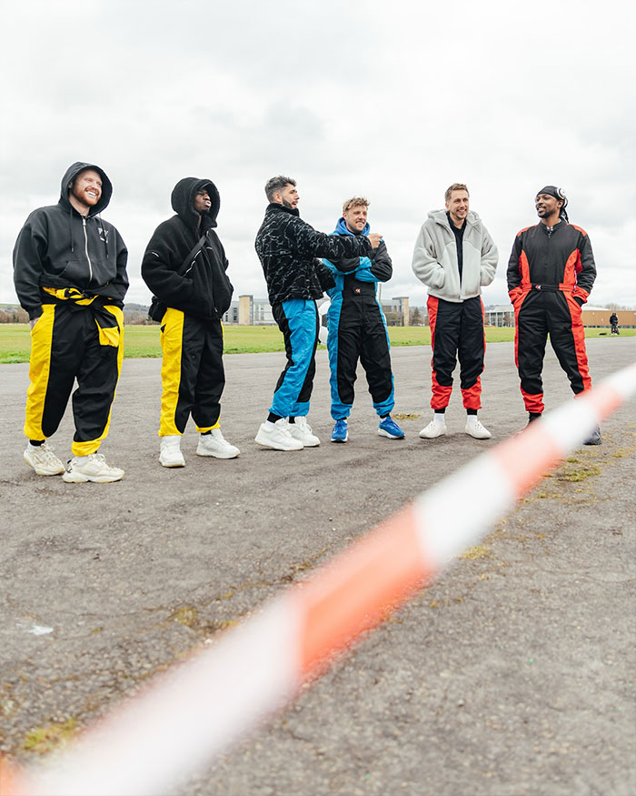 Group of men dressed in colorful racing suits standing outdoors, relating to KSI&rsquo;s net worth and Prime stake discussion.