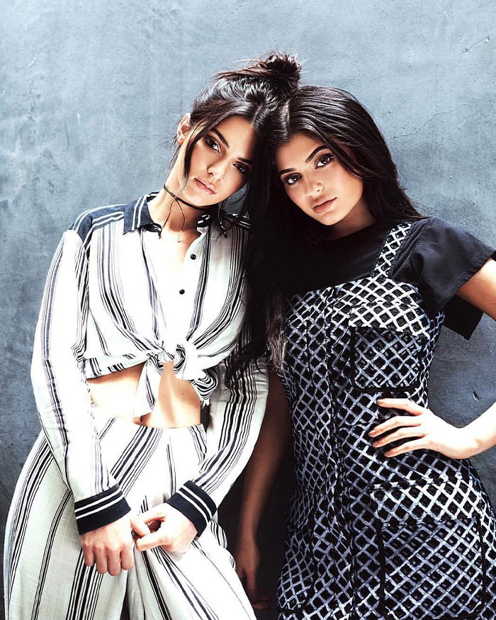 Two women posing stylishly against a textured wall, illustrating Kylie Jenner&rsquo;s net worth and financial status update.