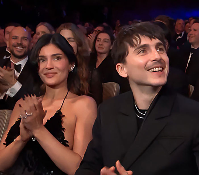 Couple dressed formally applauding at an event, unrelated to Kylie Jenner Met Gala stiletto pain incident. Couple dressed formally applauding at an event, unrelated to Kylie Jenner Met Gala stiletto pain incident.