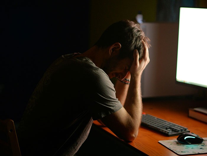 Man sitting at a desk with head in hands, appearing stressed over missing iPad and family tension at night.