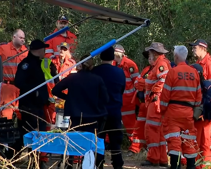 Search and rescue team in orange uniforms gathers outdoors near a wooded area during a teen disappearance investigation.