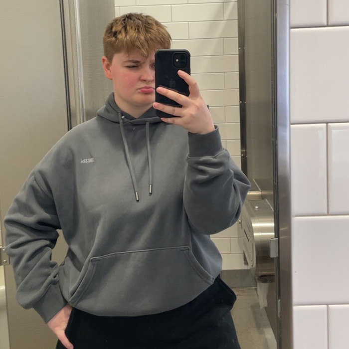 Person taking a mirror selfie in a bathroom wearing a gray hoodie, related to lesbian beaten unconscious McDonald's bathroom incident.