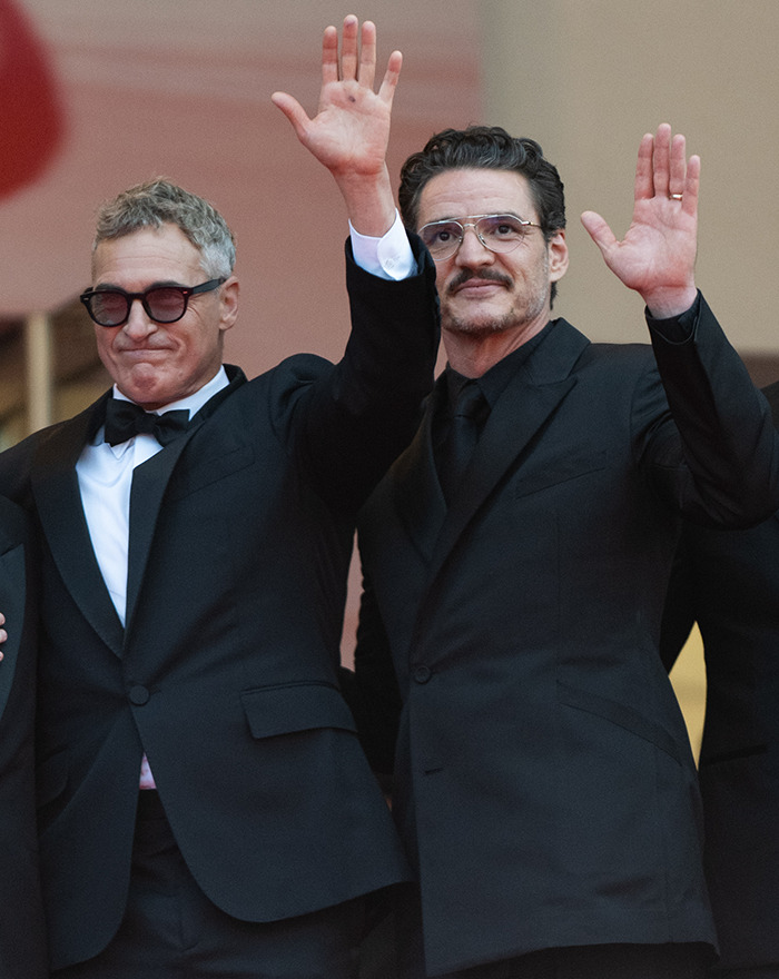 Pedro Pascal and Joaquin Phoenix in formal suits waving, with lip reader decoding their interaction.
