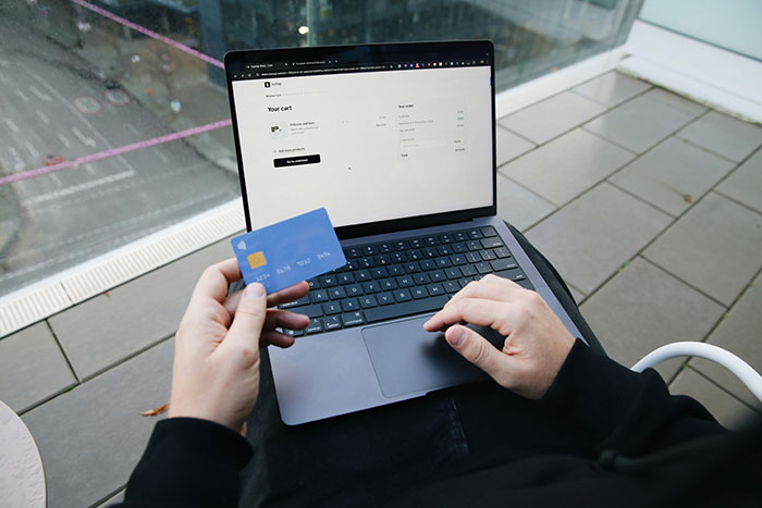 Person using laptop and holding a credit card, illustrating how people use the anonymity of the internet to share secrets.