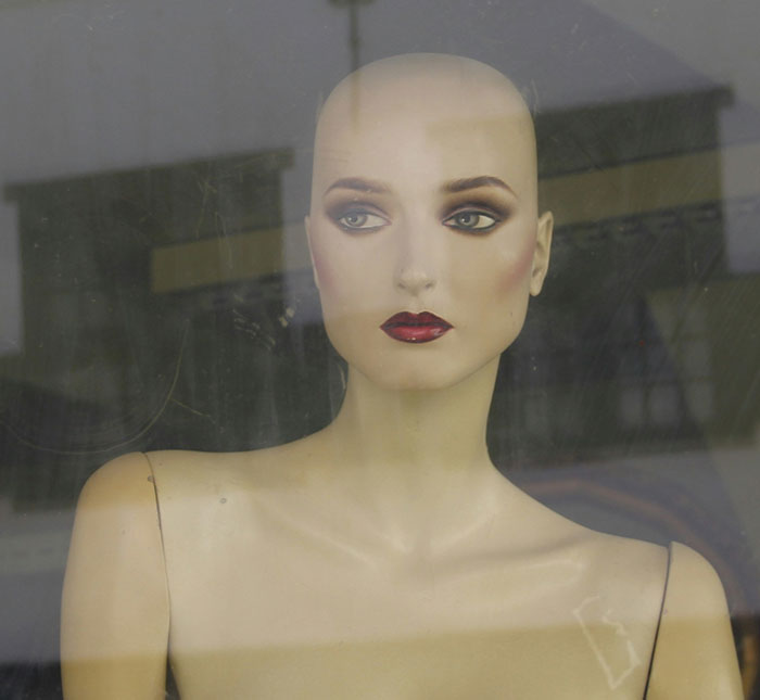 Mannequin with dramatic makeup behind glass, symbolizing anonymity people use to share dirty secrets online.