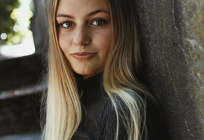 Young woman with long blonde hair leaning against a wall, representing people using internet anonymity to share secrets.