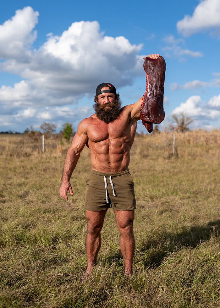 Muscular man outdoors holding a large raw animal liver, promoting extreme raw animal diet in a sunny field setting. Muscular man outdoors holding a large raw animal liver, promoting extreme raw animal diet in a sunny field setting.