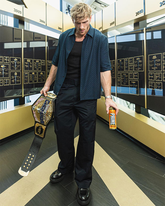 Logan Paul holding a championship belt and a can of Prime drink, highlighting Logan Paul net worth after Prime.