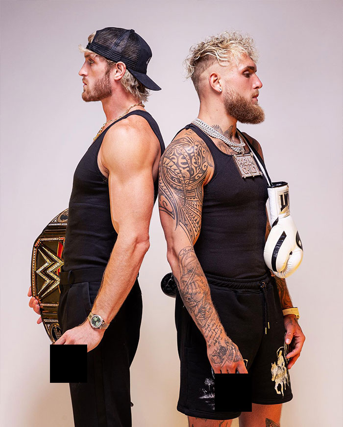 Logan Paul standing back to back with shirtless tattooed man holding boxing glove and championship belt.