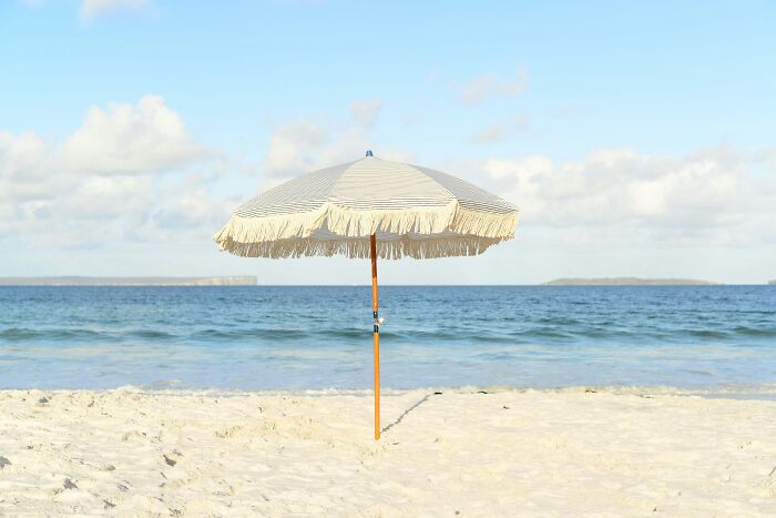 Beach umbrella on sandy shore near ocean waves, illustrating casual things that can be deadly in unexpected ways.